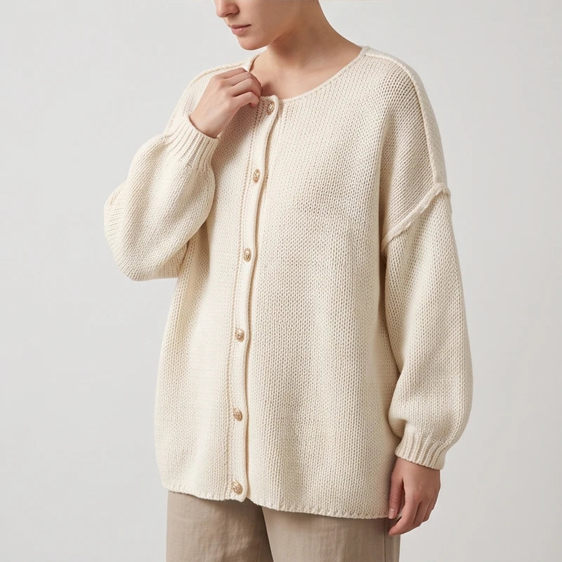 Woman wearing an oversized cream knit cardigan with dropped shoulders, puff sleeves, and gold-rimmed buttons, over tan pants.