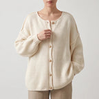 Woman wearing an oversized cream knit cardigan with light brown buttons, loosely holding the front edge.