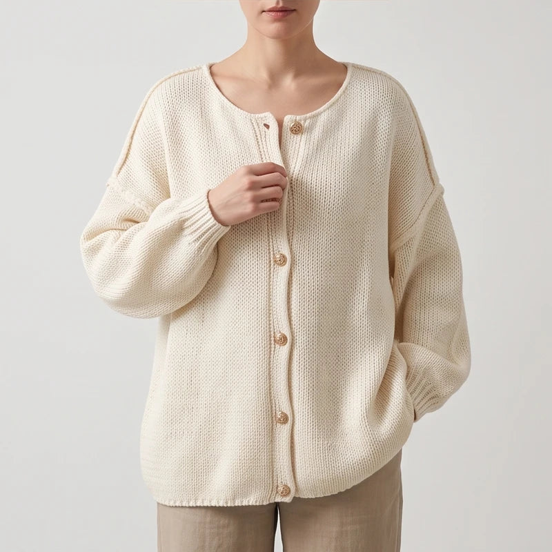 Woman wearing an oversized cream knit cardigan with light brown buttons, loosely holding the front edge.