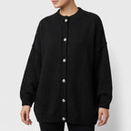 Woman wearing a black oversized knit cardigan with a ribbed collar and cuffs, featuring five large silver-toned buttons down the front.