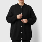 Woman wearing a black knit cardigan with large, decorative silver buttons and ribbed cuffs, adjusting the front.