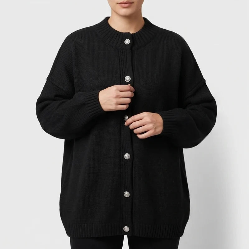 Woman wearing a black knit cardigan with large, decorative silver buttons and ribbed cuffs, adjusting the front.