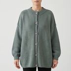 Woman wearing an oversized sage green knit cardigan with ribbed collar, cuffs, and silver-tone buttons, on a white background.