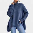 Woman wearing a soft, oversized indigo blue turtleneck sweater with ribbed cuffs and a high-low hem, paired with jeans.
