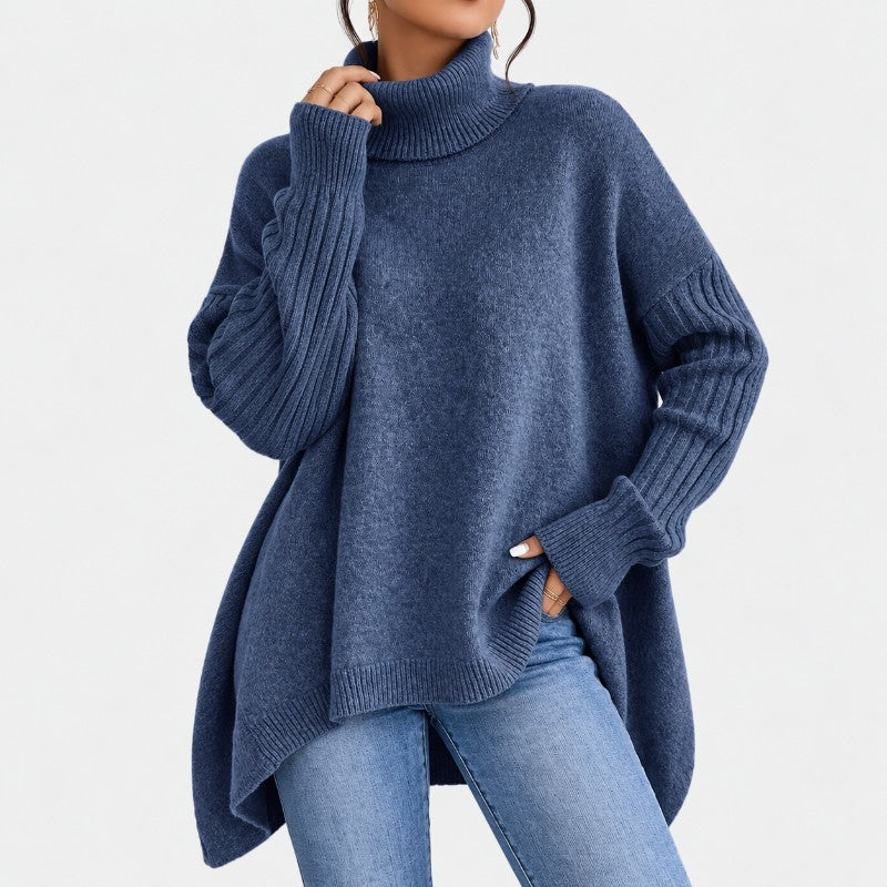 Woman wearing a soft, oversized indigo blue turtleneck sweater with ribbed cuffs and a high-low hem, paired with jeans.