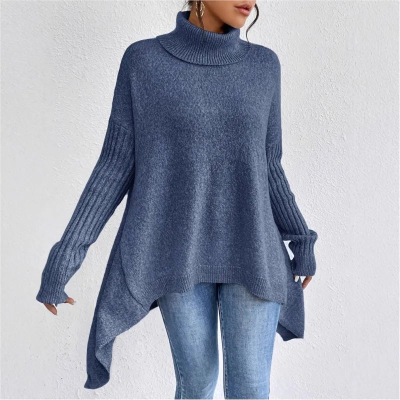 Woman wearing a slate blue oversized knit turtleneck sweater with ribbed sleeves and an asymmetrical hem, paired with blue jeans.