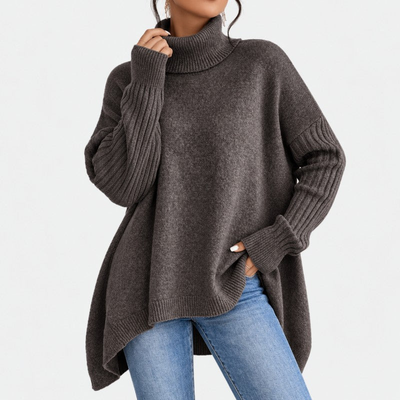 Woman wearing a dark gray oversized knit turtleneck sweater with ribbed cuffs and a high-low hem, paired with blue jeans.