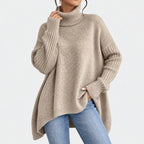 Woman wearing a loose-fitting beige knit turtleneck sweater with ribbed cuffs and hem, styled with blue jeans.