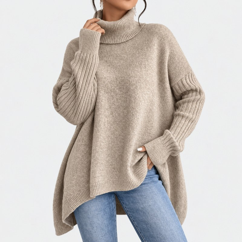 Woman wearing a loose-fitting beige knit turtleneck sweater with ribbed cuffs and hem, styled with blue jeans.
