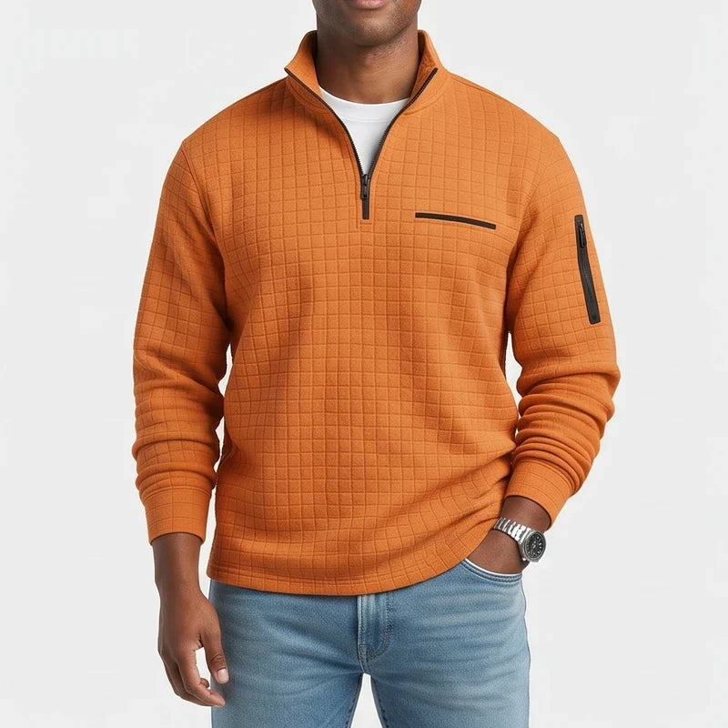 Man wearing an orange quarter-zip waffle knit jumper with black chest and arm zipper pockets, paired with blue jeans.