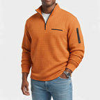 Man wearing an orange waffle-knit quarter-zip pullover with a chest pocket and arm zipper, paired with light blue jeans.