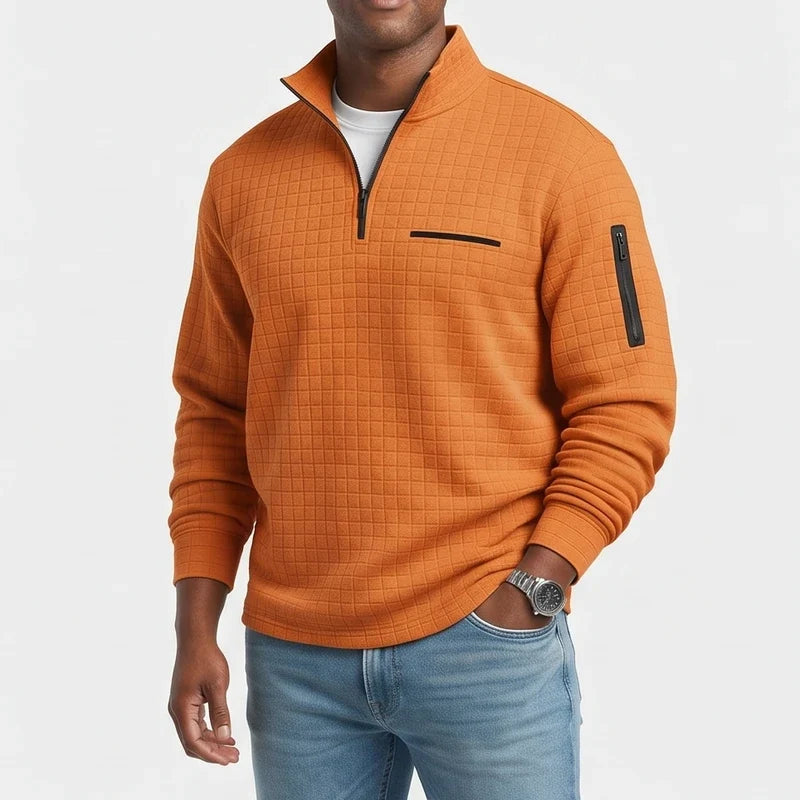 Man wearing an orange waffle-knit quarter-zip pullover with a chest pocket and arm zipper, paired with light blue jeans.