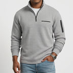 Man wearing a light gray waffle knit quarter-zip jumper with black zippers and a chest pocket, paired with blue jeans.