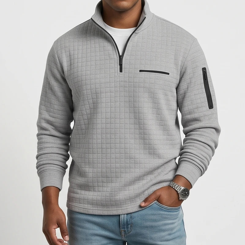 Man wearing a light gray waffle knit quarter-zip jumper with black zippers and a chest pocket, paired with blue jeans.