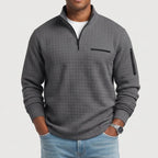 Man wearing a gray waffle knit quarter-zip jumper with a black zipper, a chest pocket, and a sleeve pocket.