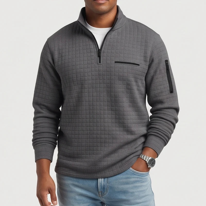 Man wearing a dark grey quilted quarter-zip pullover with a chest pocket and arm pocket, light wash jeans.