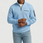 Man wearing a light blue quilted quarter-zip pullover with a black zipper, chest pocket, and sleeve pocket.