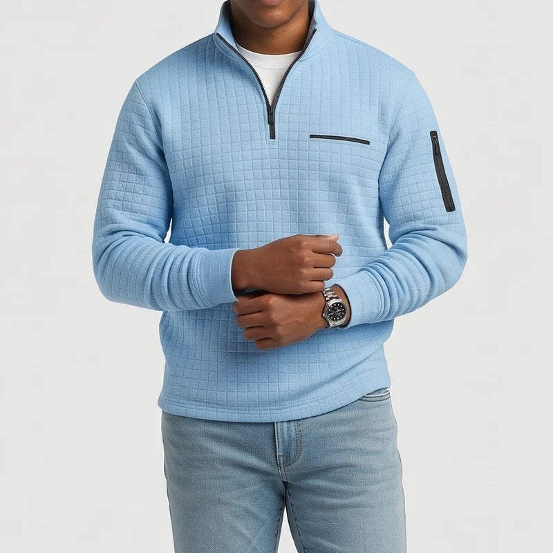 Man wearing a light blue quilted quarter-zip pullover with a black zipper, chest pocket, and sleeve pocket.