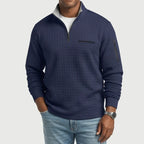 Man wearing a navy textured long-sleeve sweater with a quarter-zip collar, chest pocket, and arm pocket, paired with light jeans.