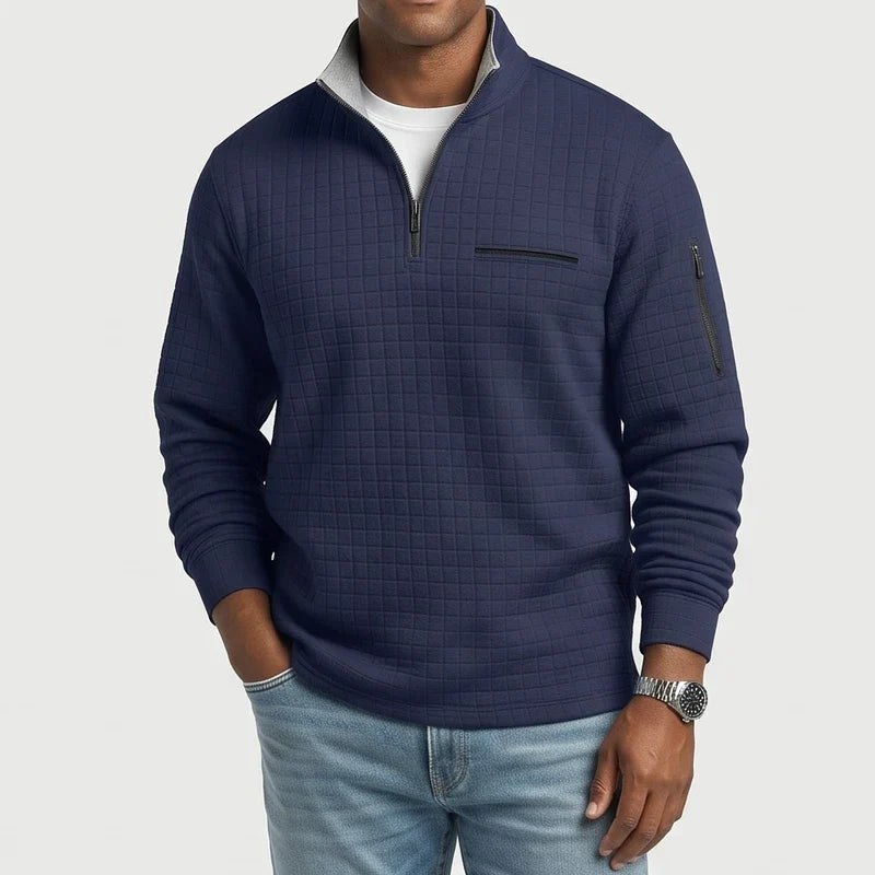 Man wearing a navy textured long-sleeve sweater with a quarter-zip collar, chest pocket, and arm pocket, paired with light jeans.