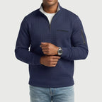 Man wearing a navy blue quilted quarter-zip pullover with a chest pocket and arm zipper, adjusting a silver watch.
