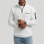 Man wearing a light grey quilted quarter-zip top with black accents, light blue jeans, and a silver watch.