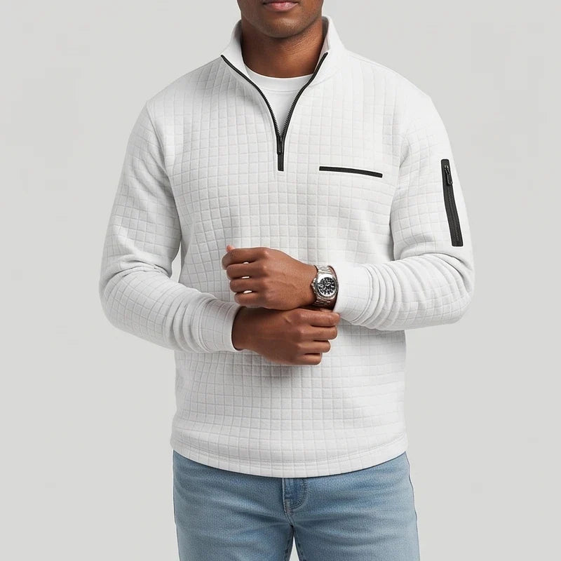 Man wearing a light grey quilted quarter-zip top with black accents, light blue jeans, and a silver watch.