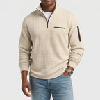 Man wearing a light beige waffle knit quarter-zip jumper with a black zipper and a zippered pocket on the sleeve.