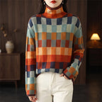 Woman wearing a colorful checked turtleneck sweater with red, orange, blue, and green squares, paired with white pants.