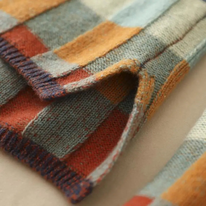 Close-up of a chunky knit checked jumper in grey, rust orange, and blue with ribbed cuffs and hem.