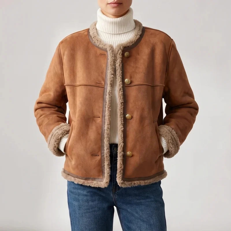 Woman wearing a collarless brown jacket with visible cream shearling lining, gold buttons, and hands in pockets, against a white background.