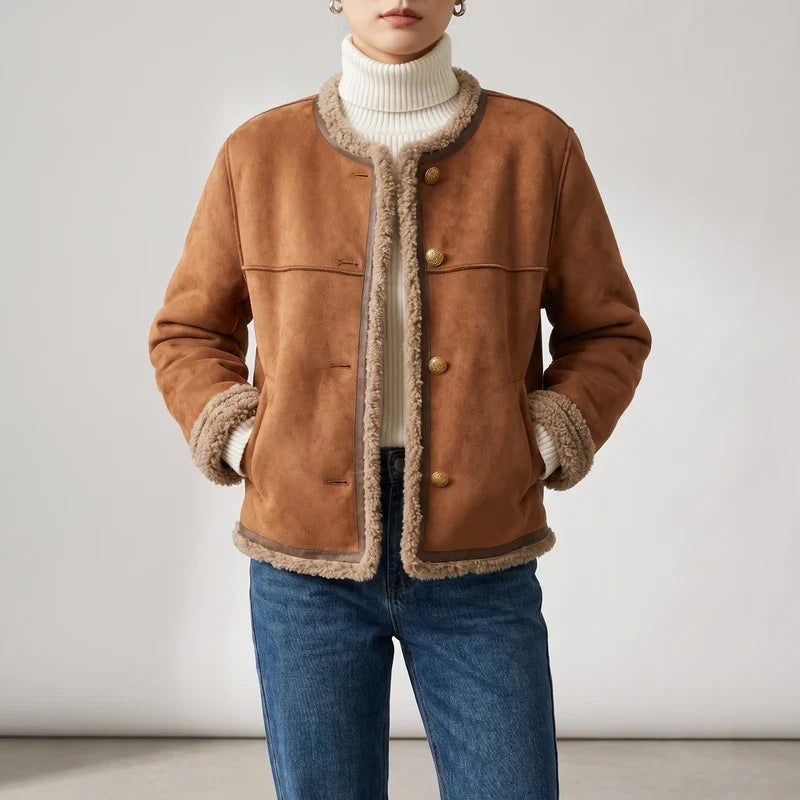 Woman wearing a brown suede jacket with shearling lining, gold buttons, and dark trim over a white turtleneck and blue jeans.