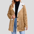 Woman wearing a tan suede-feel jacket with white borg lining, exposed collar, three dark buttons, and two patch pockets.