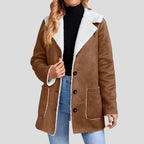 Woman wearing a brown suede-look blazer jacket with white borg lining, open over a black turtleneck and blue jeans.