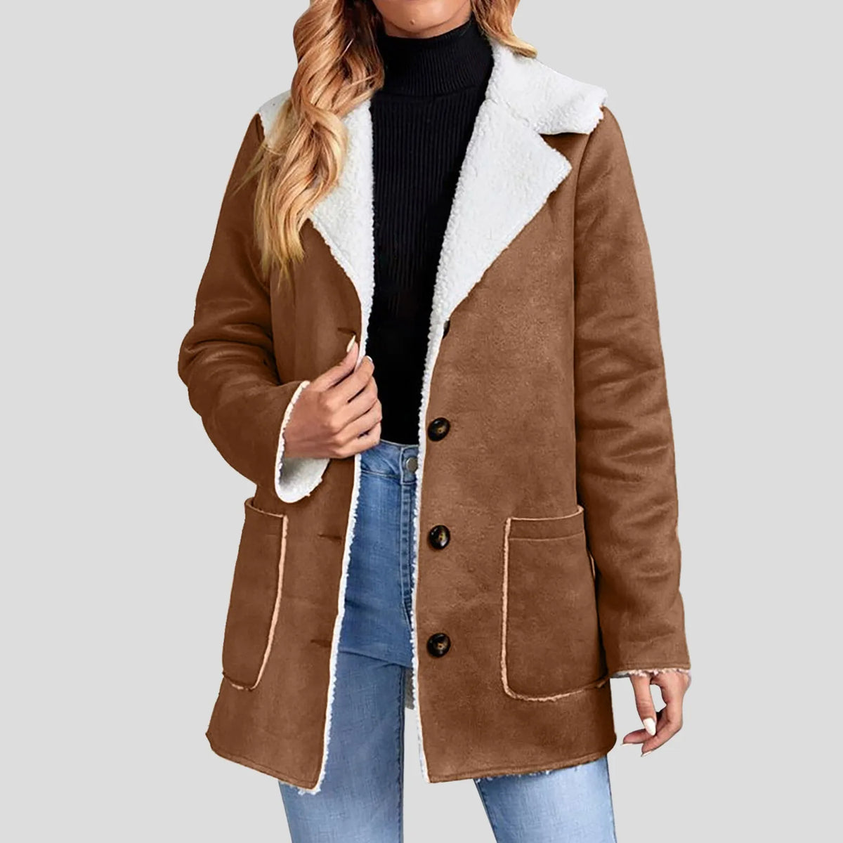 Woman wearing a brown suede-look blazer jacket with white borg lining, open over a black turtleneck and blue jeans.
