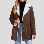 Woman wearing a brown suede-look jacket with white fuzzy borg lining, black turtleneck, and blue jeans.