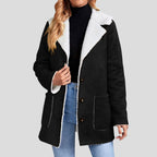 Woman wearing a black suede-like jacket with a white borg lining and collar, styled open over a black turtleneck and jeans.