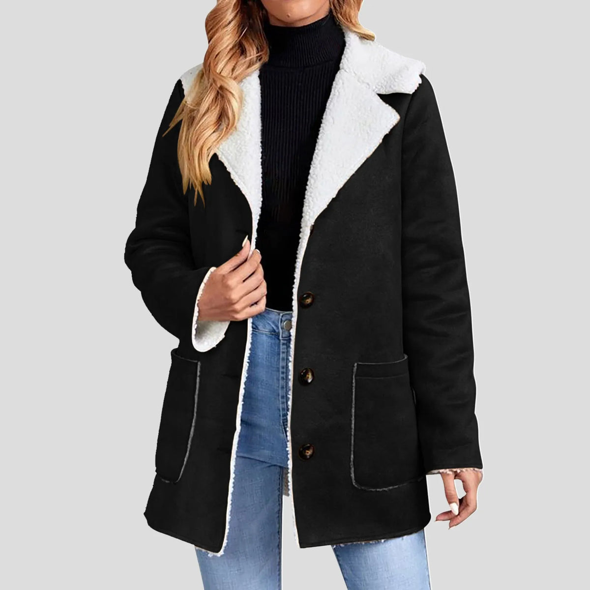 Woman wearing a black suede-like jacket with a white borg lining and collar, styled open over a black turtleneck and jeans.