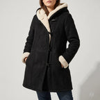 Woman wearing a black suede-look duffle coat with creamy borg lining, toggle closures, and hands in pockets.