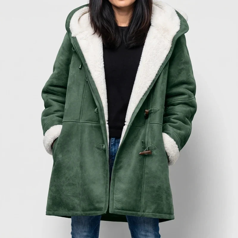 Woman wearing a long, green suede duffle coat with white borg lining and distinctive brown toggle closures, against a white background.