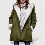 Woman wearing an olive green hooded coat with white borg lining and dark toggle closures, over a gray turtleneck.