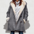 Woman wearing an unzipped gray suede borg-lined coat with toggle closures over a light gray turtleneck, hands in pockets.