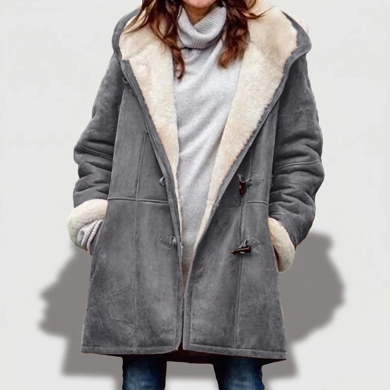 Woman wearing an unzipped gray suede borg-lined coat with toggle closures over a light gray turtleneck, hands in pockets.