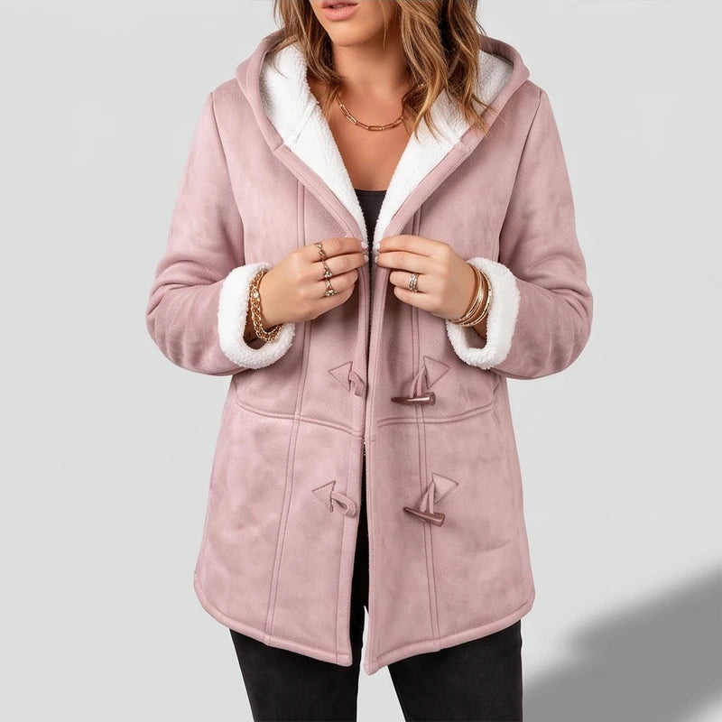 Woman adjusting a pink suede-like hooded coat with white borg lining and brown toggle closures, wearing rings and bracelets.