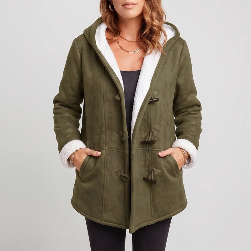 Woman wearing an olive green hooded jacket with fluffy white lining, toggle closures, and hands in pockets.
