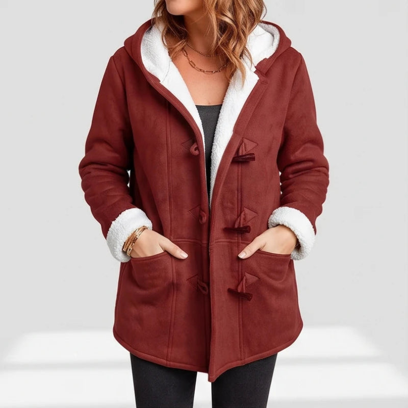 Woman wearing a rust-red faux suede jacket with a white borg-lined hood and cuffs, featuring toggle closures and front pockets.