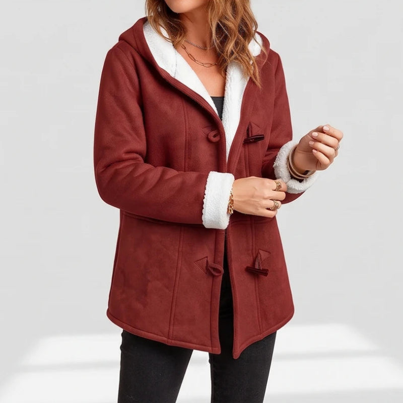 Woman wearing a reddish-brown hooded jacket with white borg lining, toggles, and rolled cuffs, adjusting her left sleeve.