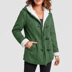 Woman wearing a green hooded coat with white sherpa lining, dark toggle closures, and hand in a pocket.
