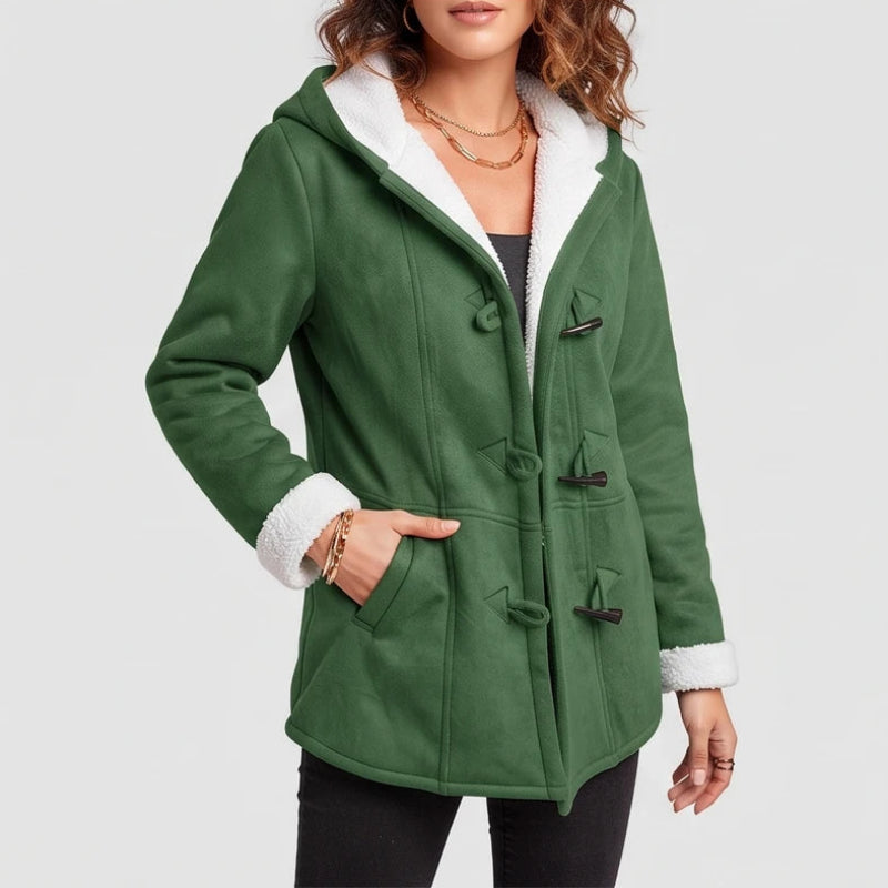 Woman wearing a green hooded coat with white sherpa lining, dark toggle closures, and hand in a pocket.