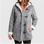 Woman wearing a grey hooded coat with visible white borg lining, dark toggle closures, and her hands in pockets.